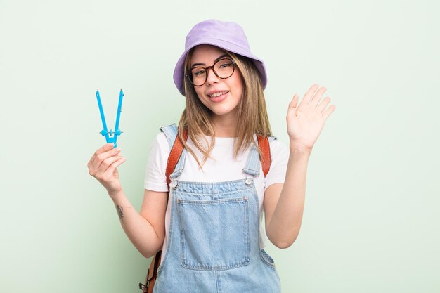 Jolie jeune femme souriante agitant joyeusement la main vous accueillant et vous saluant concept d'étudiant