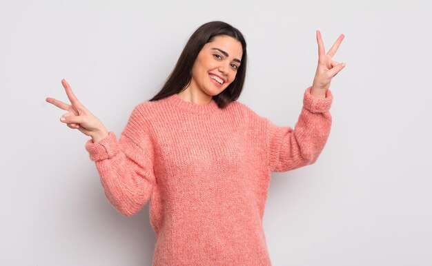 Jolie jeune femme souriante et ayant l'air heureuse, amicale et satisfaite, faisant des gestes de victoire ou de paix à deux mains