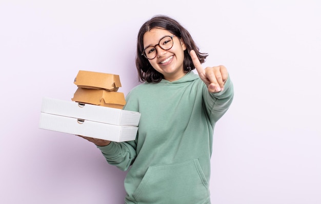 Jolie jeune femme souriante fièrement et en toute confiance faisant numéro un. concept de restauration rapide à emporter