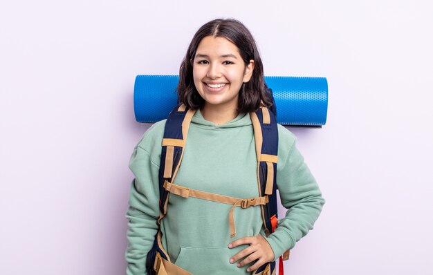 Jolie jeune femme souriante joyeusement avec une main sur la hanche et confiante. concept de randonnée