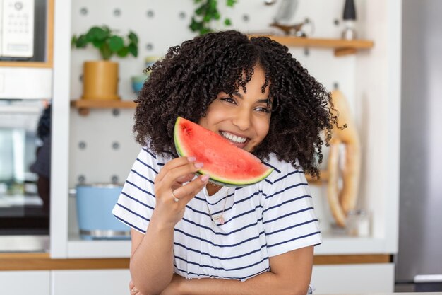 Jolie jeune femme souriante mangeant de la pastèque femme tenant une tranche de pastèque