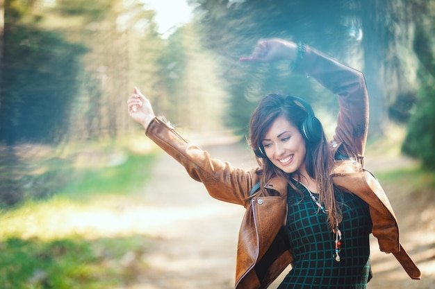 Une jolie jeune femme souriante marche le long d'un chemin forestier au début du printemps ensoleillé, s'amuse et écoute de la musique.