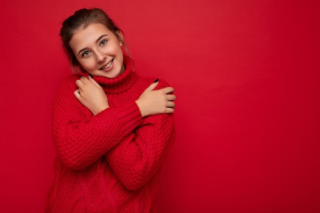 Jolie jeune femme souriante mignonne portant un pull rouge chaud isolé sur rouge