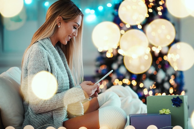 Jolie jeune femme souriante utilisant une tablette et un sourire heureux pendant les vacances de Noël confortables à la maison.