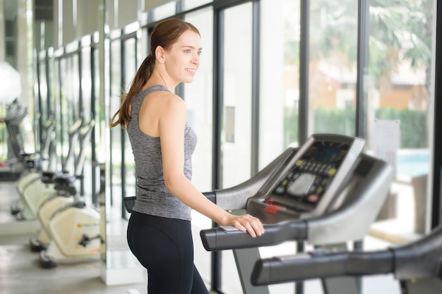 Jolie jeune femme de sport s'exécute sur tapis roulant dans la salle de gym