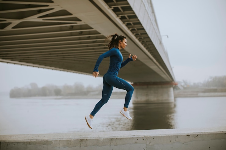 Photo jolie jeune femme en survêtement bleu courant au bord de la rivière au matin d'automne