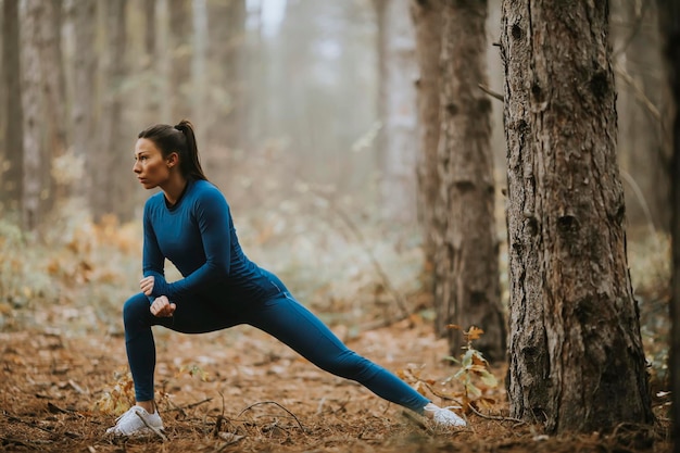 Jolie jeune femme en survêtement bleu qui s'étend avant l'entraînement dans la forêt d'automne