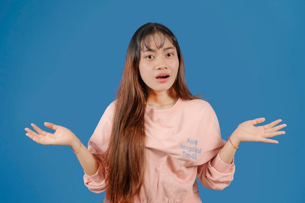 jolie jeune femme en t-shirt rose est perplexe et haussant les épaules isolé sur studio bleu