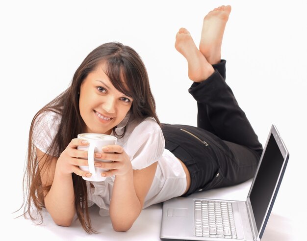 Jolie jeune femme avec une tasse de café devant un ordinateur portable ouvert