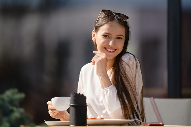 Jolie jeune femme avec une tasse de cappuccino à la main semble droite et sourit
