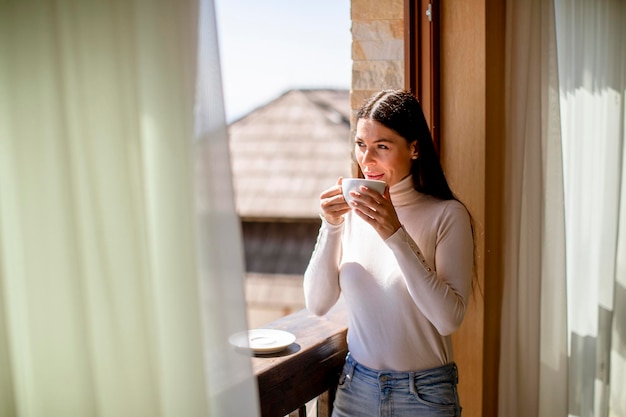 Jolie jeune femme avec une tasse de thé chaud dans la fenêtre d'hiver