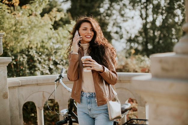 Jolie jeune femme avec téléphone portable boire du café à emporter à vélo le jour de l'automne