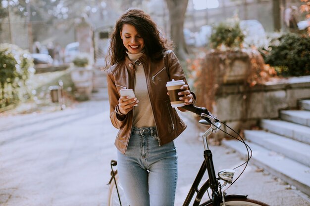 Jolie jeune femme avec téléphone portable boire du café pour aller à vélo le jour de l'automne