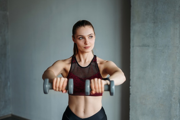 Jolie jeune femme en tenue de sport fille souriante s'entraîne avec des haltères au studio loft