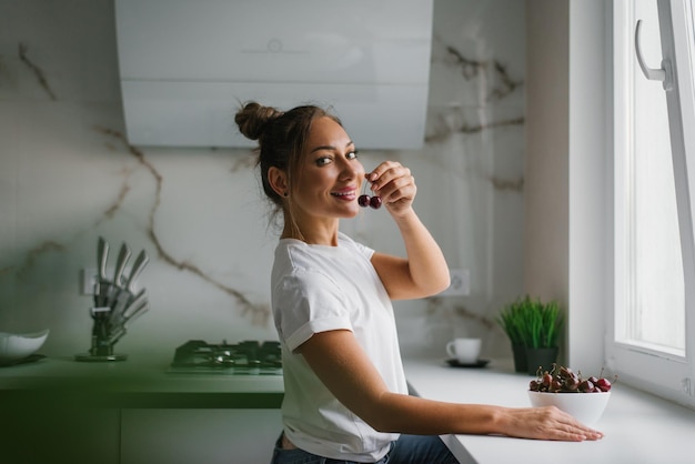 Jolie jeune femme tient une baie de cerise dans sa main et veut la manger