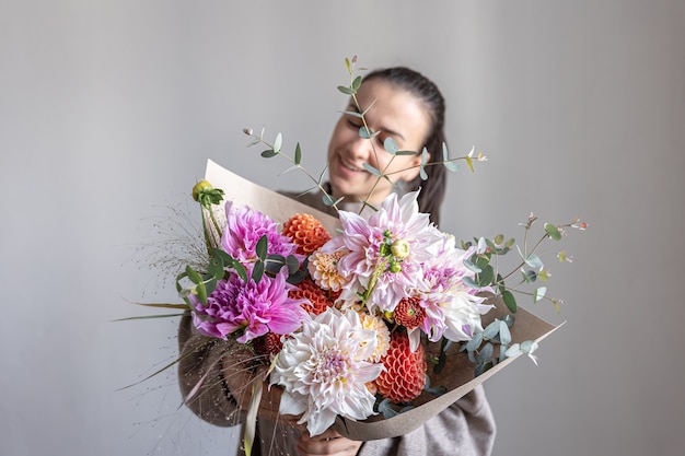 Une jolie jeune femme tient un grand bouquet de fête avec des chrysanthèmes et d'autres fleurs dans ses mains.