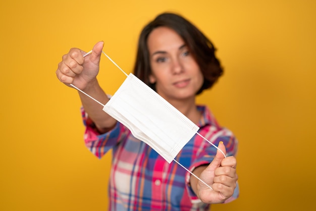 Jolie jeune femme tient un masque de protection au premier plan isolé sur fond jaune concept de quarantaine...