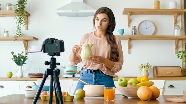 Une jolie jeune femme en train de tourner un blog sur la cuisine. Blog vidéo sur l'alimentation saine. Jolie femme parle et cuisine sur la caméra. La femme diffuse un Vlog vidéo en ligne.