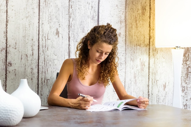 Jolie jeune femme travaillant sur des mots croisés à la maison dans un magazine assis à une table avec copyspace