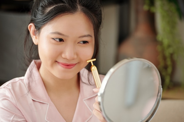 Jolie jeune femme utilisant un petit rouleau de massage lors de l'application de sérum sur sa peau