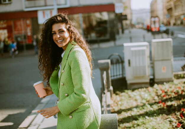 Jolie jeune femme utilisant un smartphone dans la rue et tenant du café à emporter