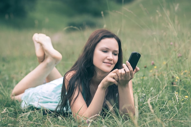 jolie jeune femme utilisant son smartphone en position couchée dans une clairière. les gens et la technologie