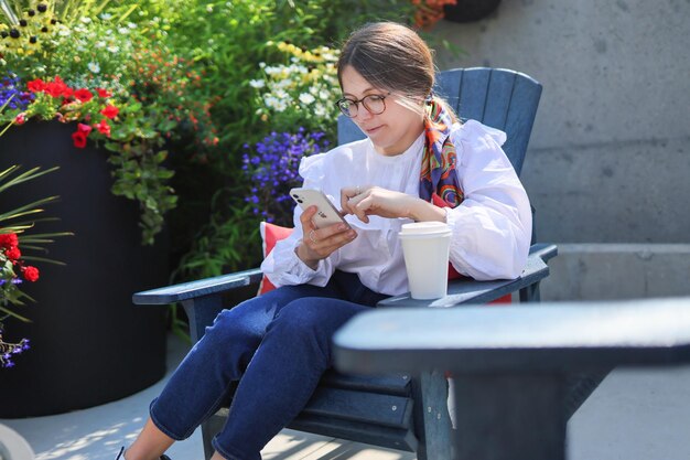 Jolie jeune femme vérifiant son téléphone dans un café en plein air fleurs sur fond