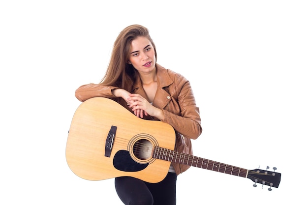 Jolie jeune femme en veste marron et pantalon noir jouant de la guitare en studio