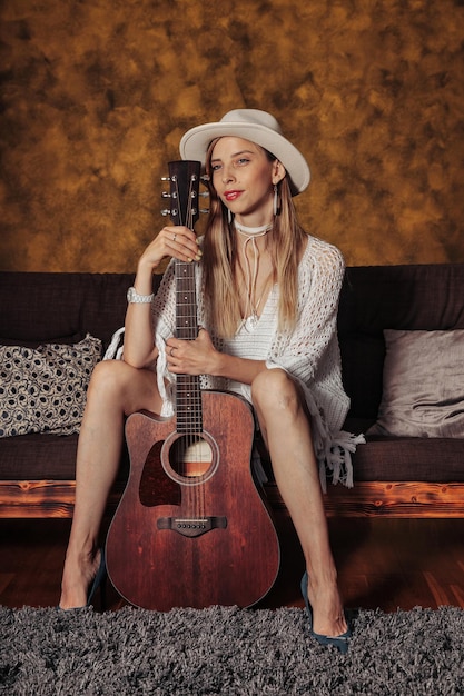 Jolie jeune femme en vêtements blancs avec guitare dans la pièce intérieure