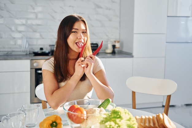 Jolie jeune femme en vêtements décontractés est assise sur la cuisine avec du poivron rouge