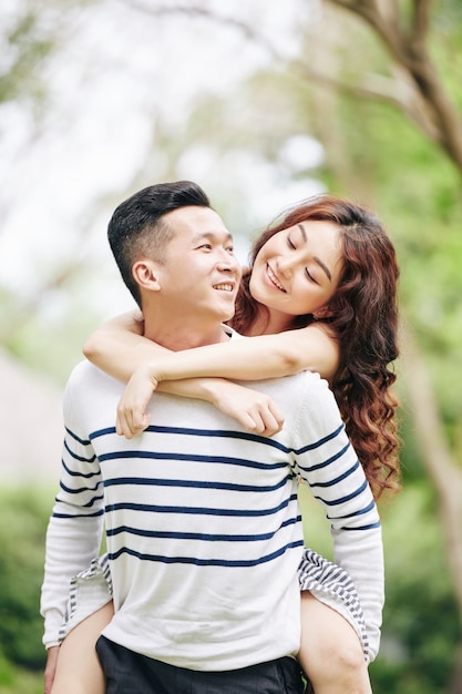 Jolie jeune femme vietnamienne amoureuse regardant son petit ami et le serrant dans ses bras quand ils se tiennent dans un parc