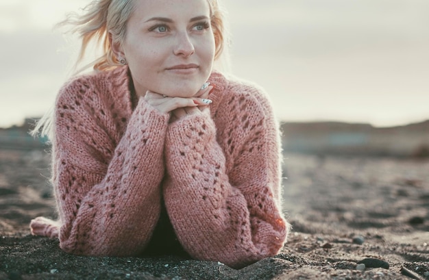 Une jolie jeune fille allongée sur le sable à la plage et regardant vers l'avenir avec une expression de rêveur sur le visage