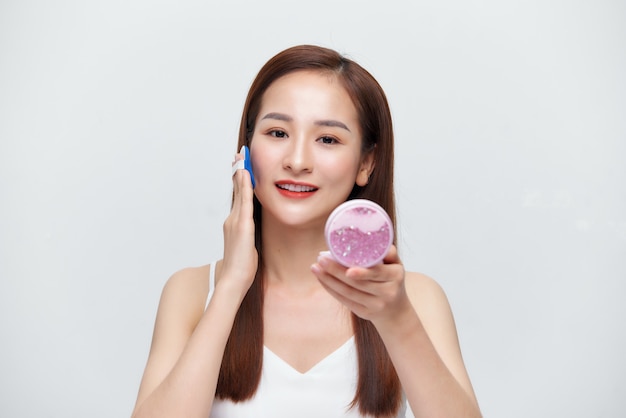Jolie jeune fille asiatique tenant un produit cosmétique en chemise blanche montrant sa peau