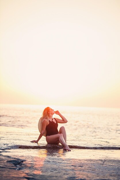 Jolie jeune fille aux cheveux longs pose devant la caméra sur la plage Elle porte un maillot de bain noir Golden sunset light