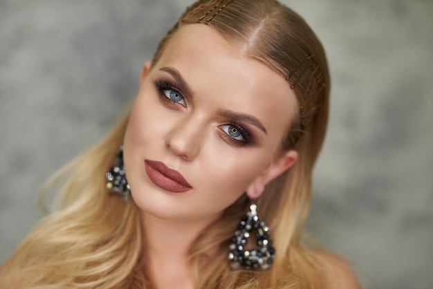 Jolie jeune fille aux cheveux recueillis. Photo d'une fille blonde avec une peau parfaite sur un mur gris. Concept de beauté et de soins de la peau