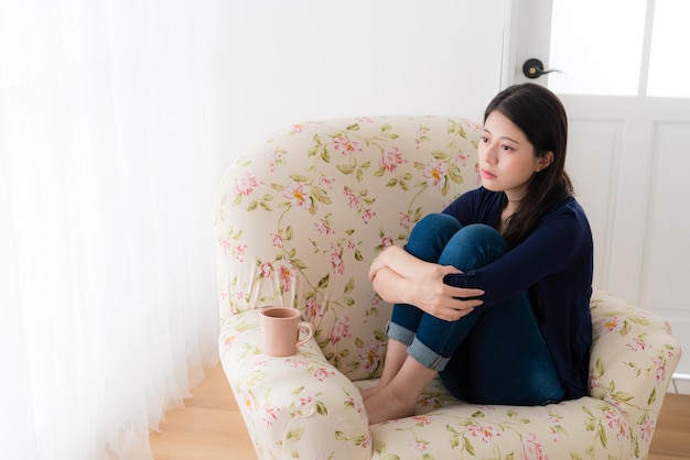 jolie jeune fille ayant un mauvais problème se sentant triste assise sur le canapé du salon se relaxant et regardant la solution de pensée de la fenêtre.