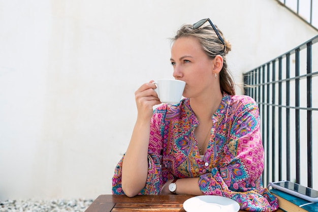 Jolie jeune fille blonde prenant un café sur la terrasse d'un bar