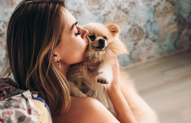 Jolie jeune fille brune embrasse son chien spitz de Poméranie.