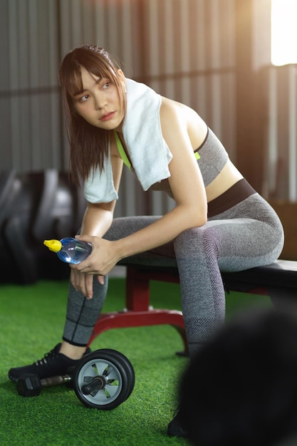 Jolie jeune fille fitness s'asseoir sur un équipement de gym avec une bouteille d'eau. reposez-vous après un entraînement intensif.