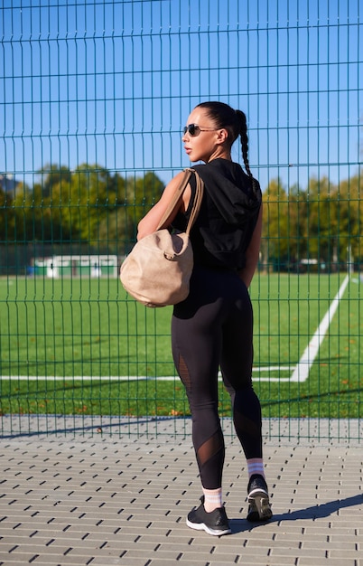 Une jolie jeune fille de fitness se prépare pour un entraînement au stade une brune attrayante et mince en survêtement avec un sac de sport va au vestiaire style de vie actif