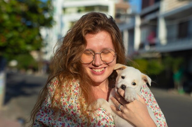 Jolie jeune fille gaie avec un chiot blanc dans ses bras petit chien marche dans la rue en été