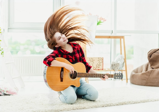 Photo une jolie jeune fille avec une guitare agitant les cheveux longs dans une chambre moderne