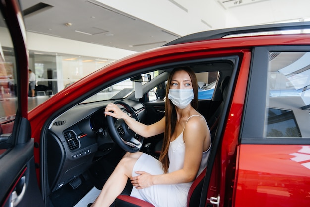 Une jolie jeune fille inspecte une nouvelle voiture chez un concessionnaire automobile dans un masque pendant la pandémie. La vente et l'achat de voitures, en période de pandémie.