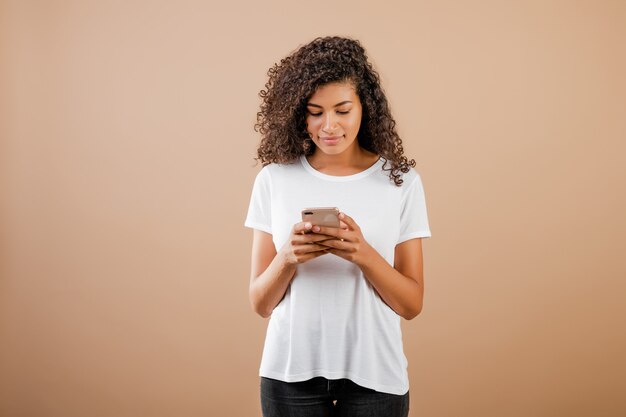 Jolie jeune fille noire avec téléphone à la main, isolée sur le marron