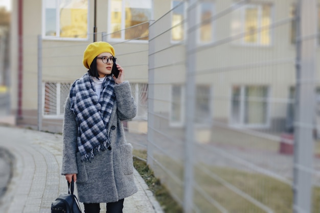 Une Jolie Jeune Fille Portant Des Lunettes De Soleil Dans Un Manteau Marchant Dans La Rue Et Parlant Au Téléphone Et Souriant