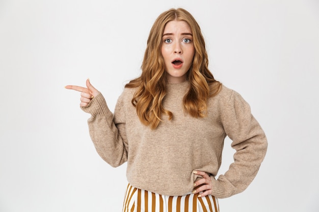 Jolie jeune fille portant un pull debout isolé sur un mur blanc, pointant vers l'espace de copie