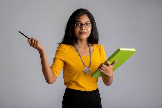 Jolie jeune fille posant avec le livre sur un mur gris