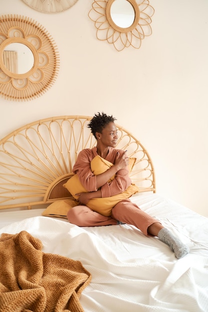 Photo une jolie jeune fille en pyjama confortable est assise sur le lit le matin, sourit et embrasse un oreiller à la maison