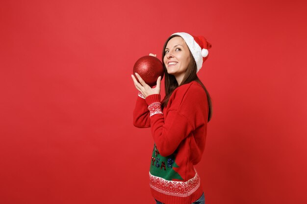 Jolie jeune fille de Santa en pull chapeau de Noël tenant un gros jouet d'arbre brillant près du visage, levant isolé sur fond rouge. Bonne année 2019 concept de fête de vacances célébration. Maquette de l'espace de copie.