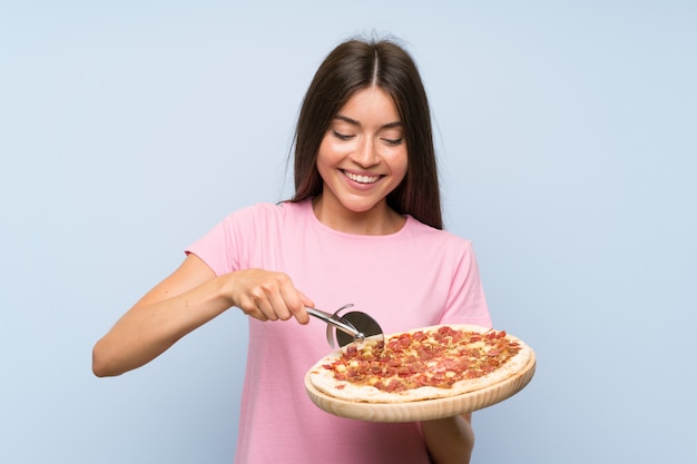 Jolie jeune fille tenant une pizza sur un mur bleu isolé